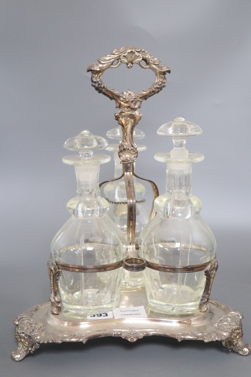 A plated three decanter tantalus of triangular form with leaf-wrapped handle, with bottles and stoppers, height 38cm